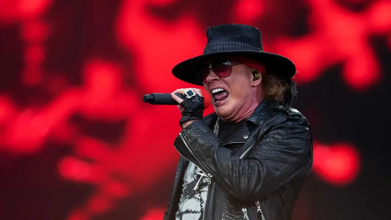 Axl Rose sjunger med en röd bakgrund. Trots rykten om axl rose sjukdom, levererar han en energisk show.
