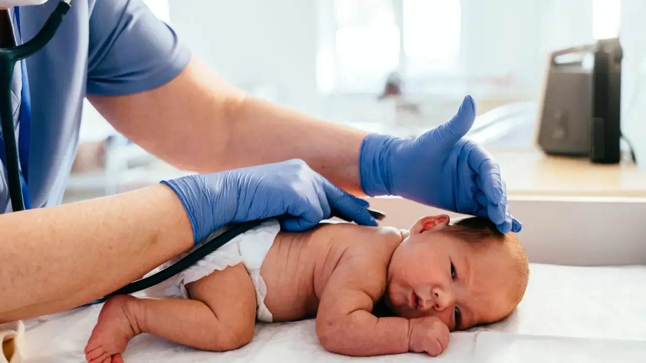 Medico controlla la schiena di un neonato, notando una piccola fossetta sacrale.