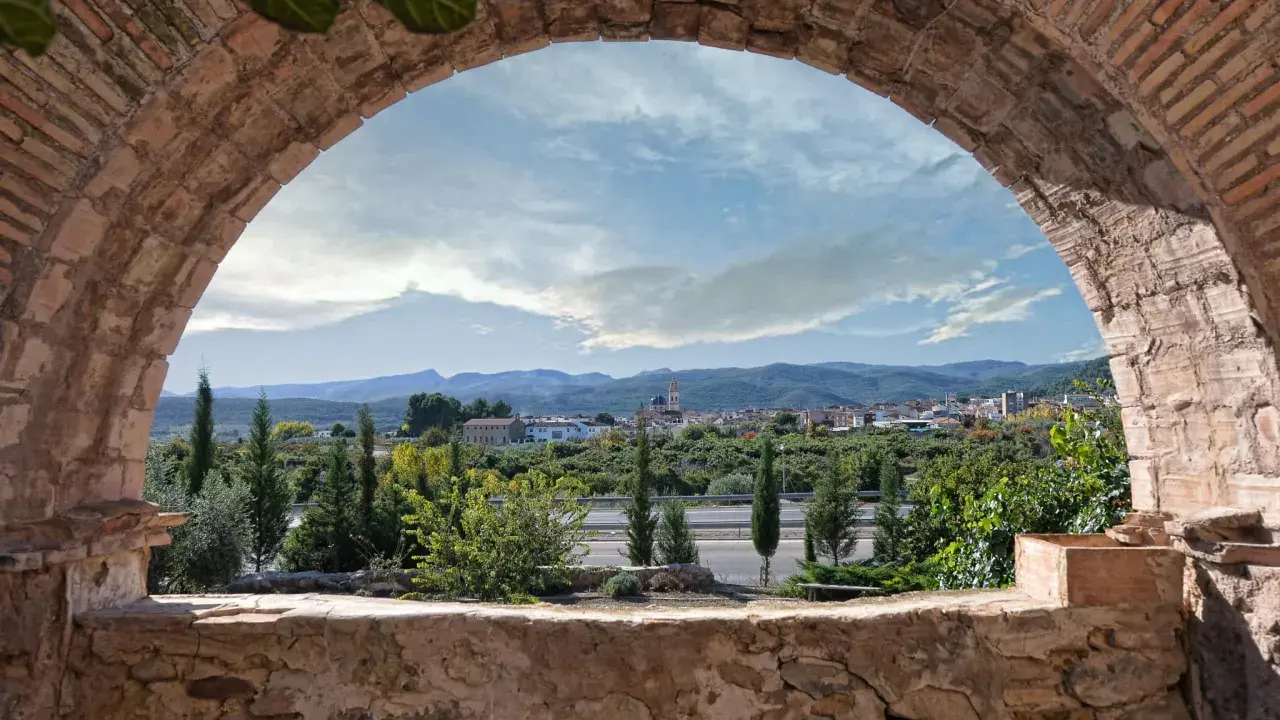 Vista de un pueblo desde un arco de ladrillo. Un paisaje con montañas y vegetación, ideal para ver en altura.