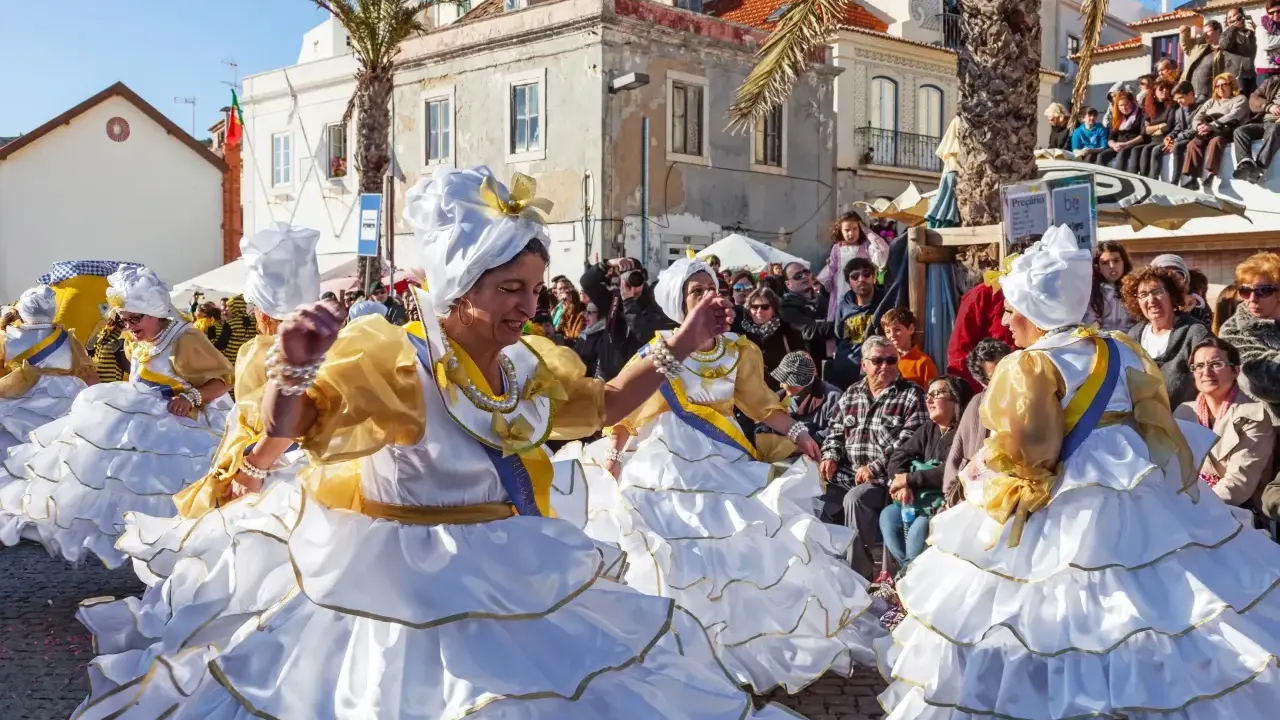 Menschen in Portugal feiern ausgelassen. Frauen in prachtvollen weißen und goldenen Kleidern mit Rüschen tanzen fröhlich.