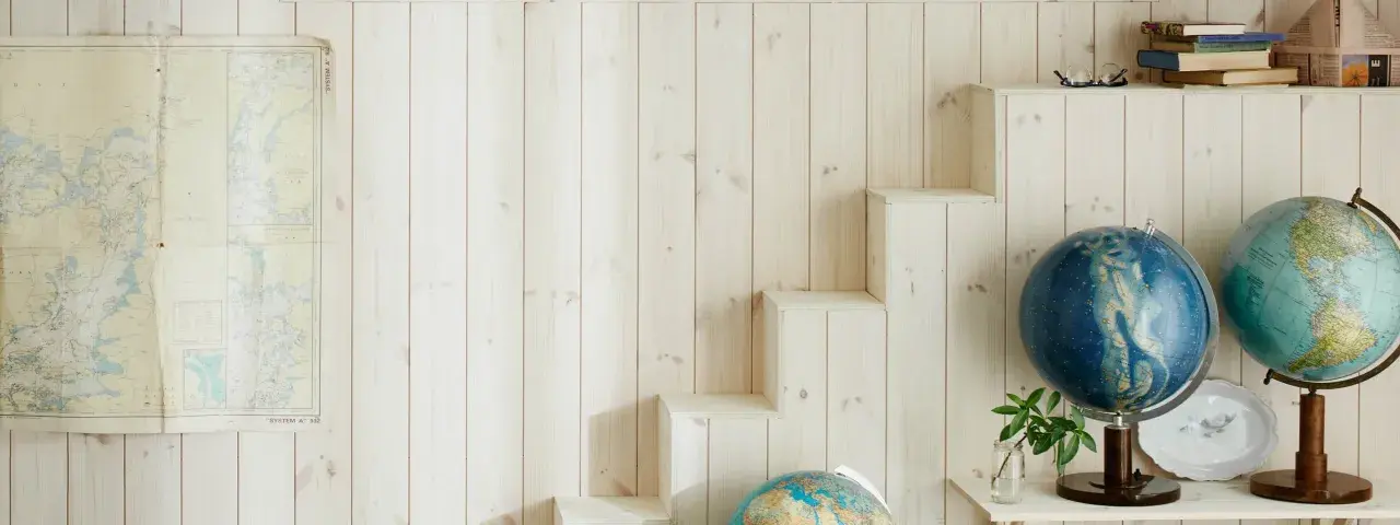 En vägg med ljus träpanel ger en mysig känsla. En gammal sjökarta hänger på ena sidan, medan en trappliknande hylla på andra sidan visar upp jordglober och böcker. Perfekt panel inomhus inspiration för äventyrliga själar.
