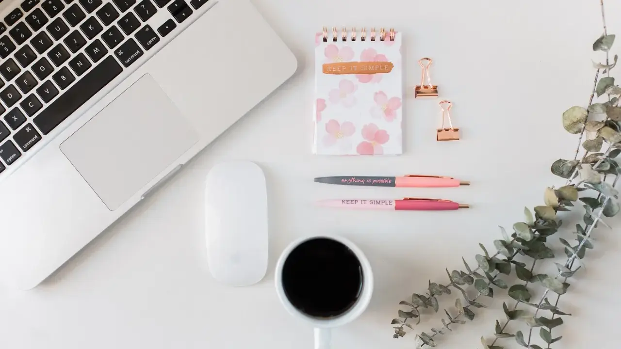 Ein Schreibtisch mit Laptop, Maus, Notizbuch, Stiften und Kaffee. Ideal für Lehrer, die ihr Zeitmanagement verbessern wollen.