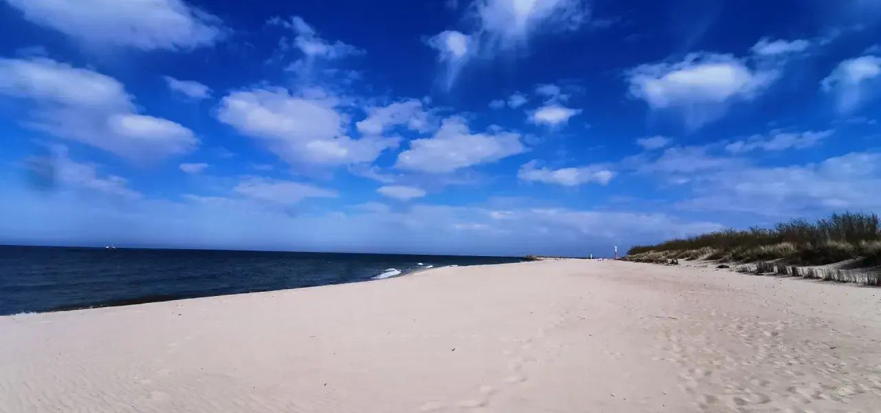 Pusta plaża z wydmami i latarnią morską, idealna na weekendowe odkrywanie magicznych miejsc nad Bałtykiem.