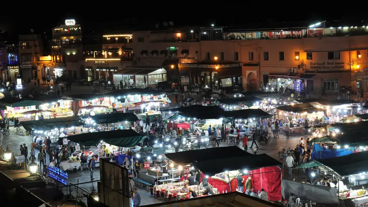 Belebter Marktplatz in Marokko bei Nacht. Viele Stände mit Lichtern und Menschen, die einkaufen und essen. Wann ist Ramadan in Marokko?