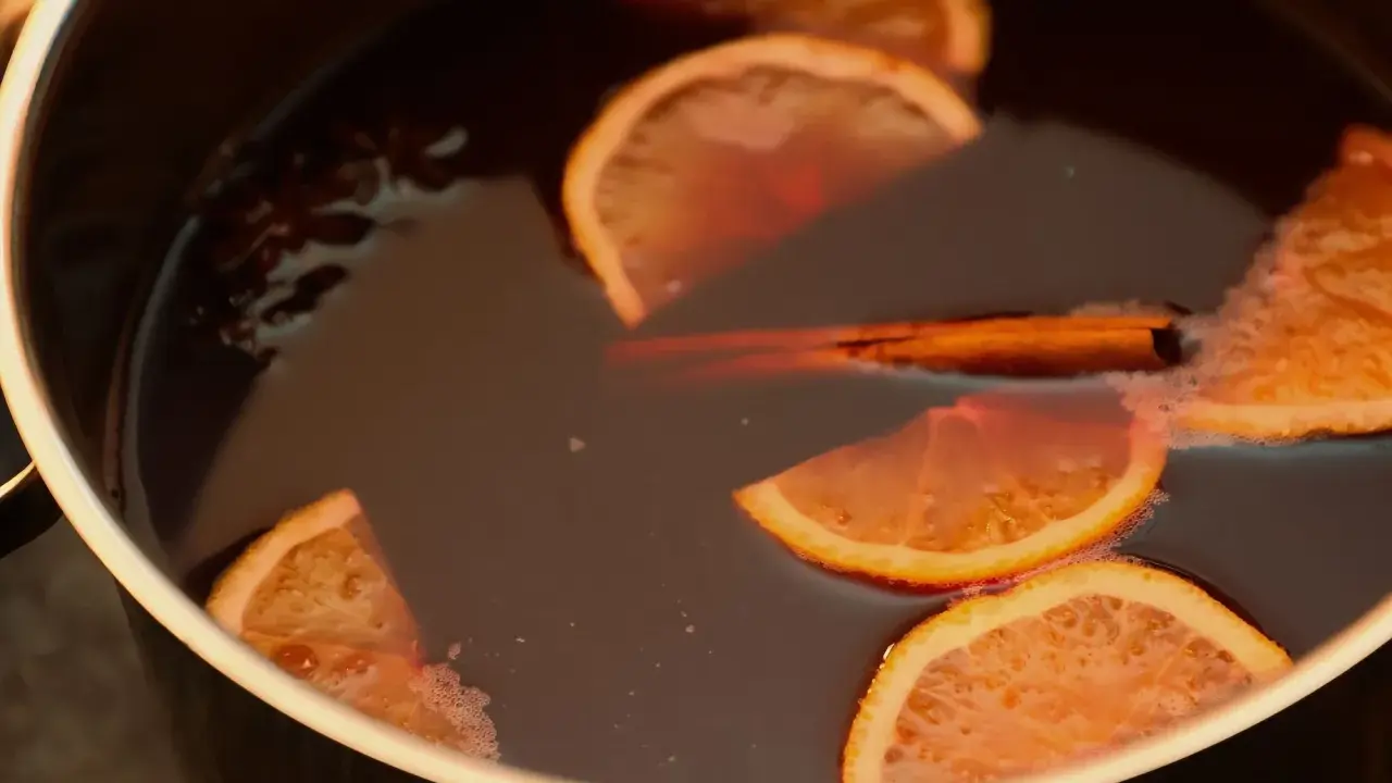 Une marmite remplie d'un liquide sombre, avec des tranches d'orange, un bâton de cannelle et de l'anis étoilé. Parfait pour une recette punch simple et réconfortante.