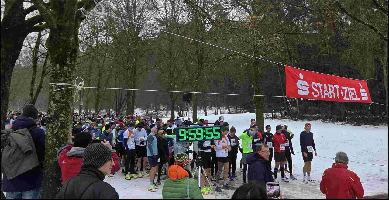 Läufer warten am Start-Ziel-Bogen für einen ultra marathon. Eine digitale Uhr zeigt 9:59:55.