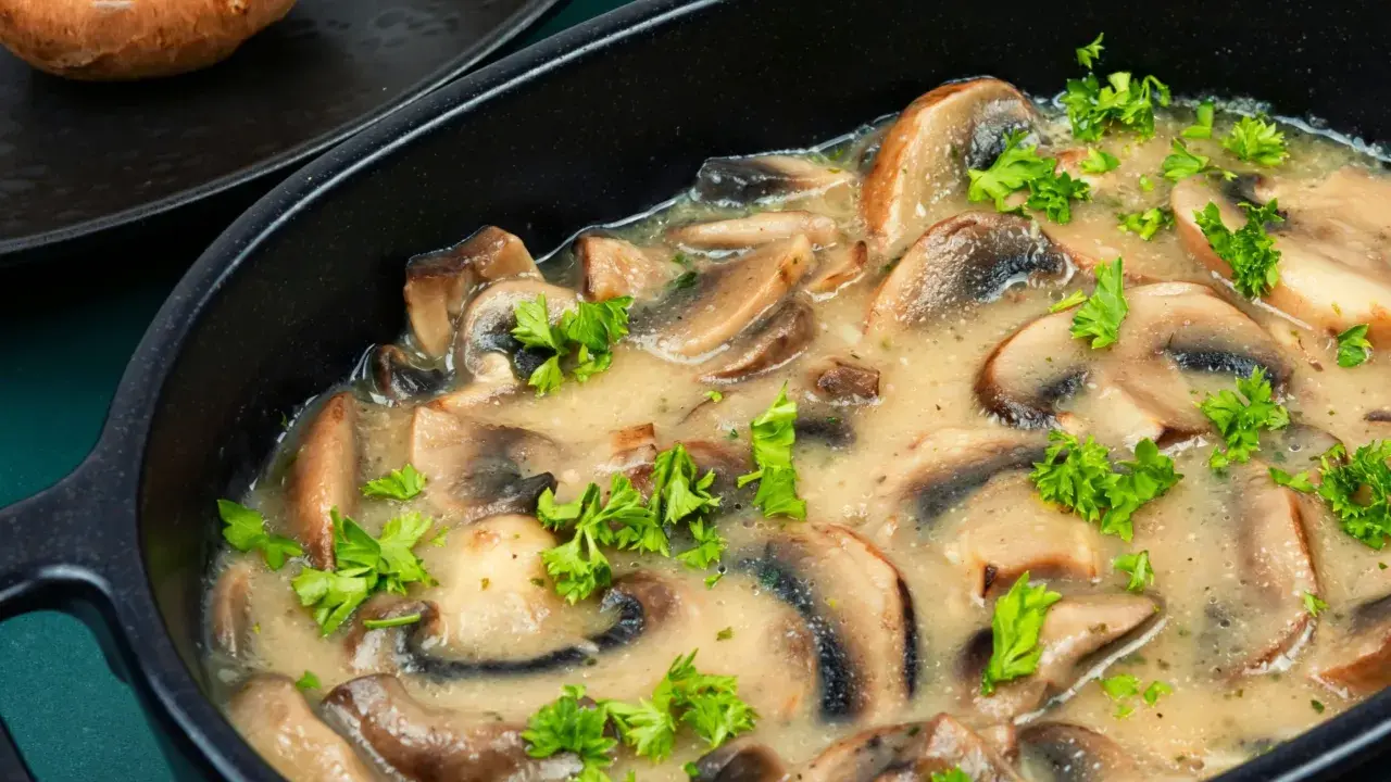 Pyszne pieczarki w śmietanie, doprawione świeżą natką pietruszki, podane w czarnej, owalnej misie.