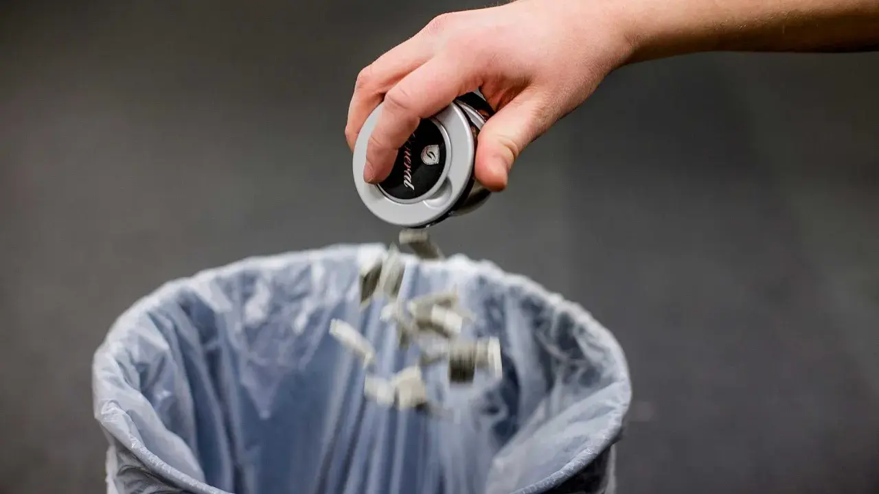 En hand tömmer snusdosan i en papperskorg. Ett steg för att sluta snusa.