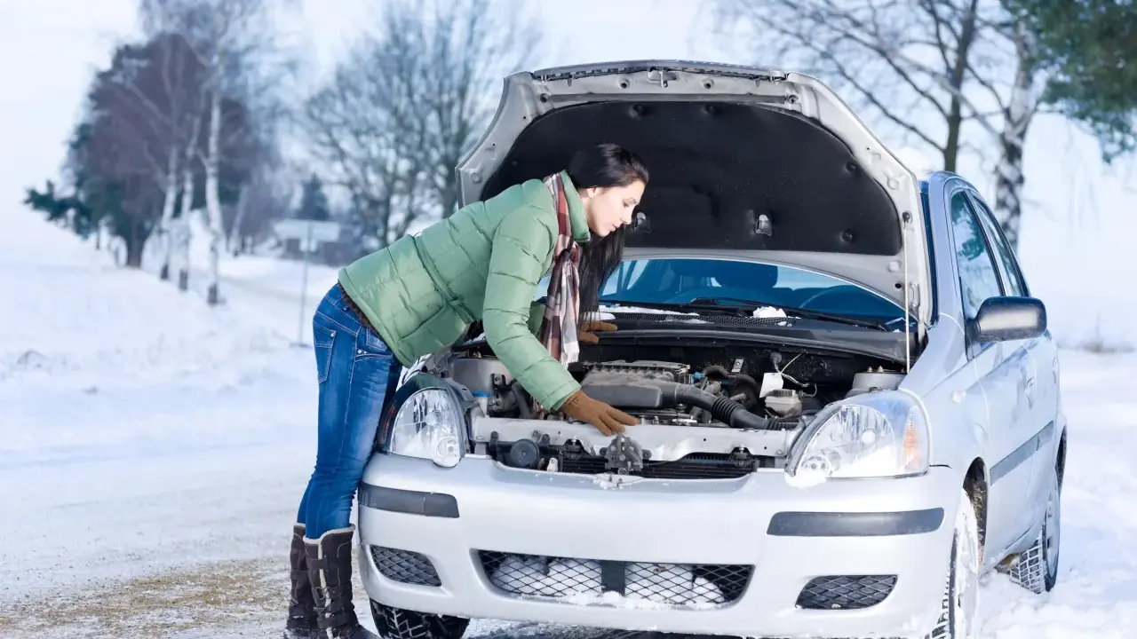 Kobieta w zimowej kurtce sprawdza silnik samochodu na śniegu. Zastanawia się, w jakiej temperaturze zamarza diesel, by uniknąć problemów.
