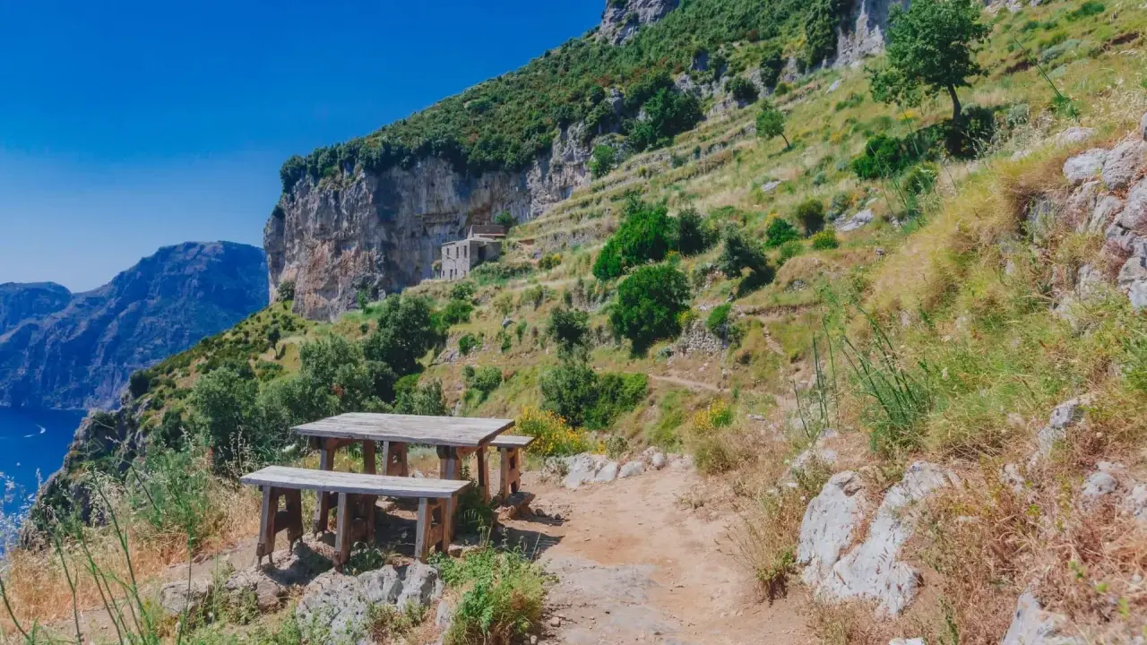 Un tavolo di legno su un sentiero roccioso, con una vista mozzafiato sul mare e sulle montagne. Un luogo perfetto per una pausa durante il cammino degli dei.