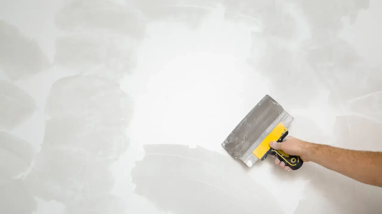 Mano con espátula aplicando masilla para alisar la pared, un paso clave en cómo quitar el gotele con espátula.
