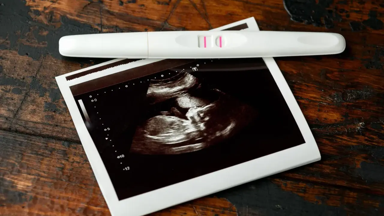 USG 7 tydzień ciąży pokazuje zarodek. Obok leży pozytywny test ciążowy.