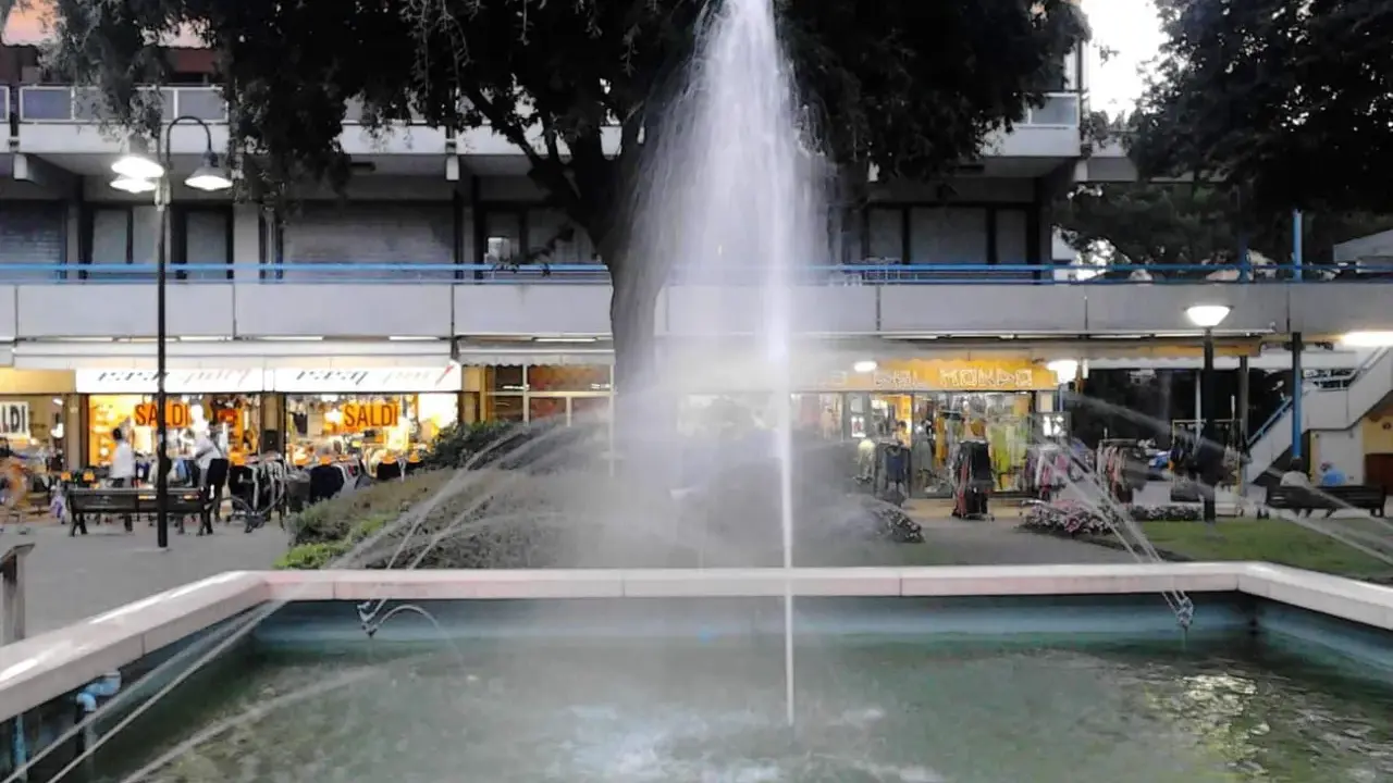 Fontana z fontanną w centrum Lido di Savio, z widokiem na sklepy i drzewa.