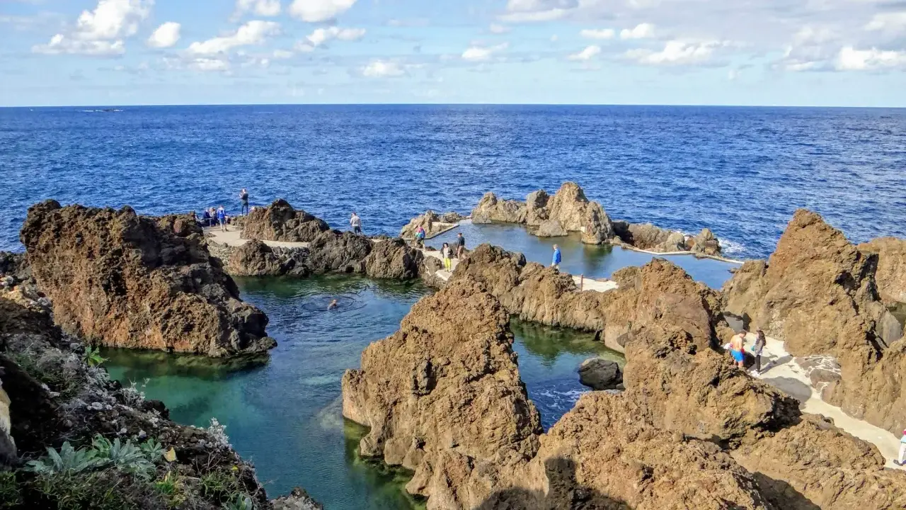 Naturschwimmbecken auf Madeira, umgeben von vulkanischem Gestein, mit Menschen, die die Sonne und das Meer genießen.
