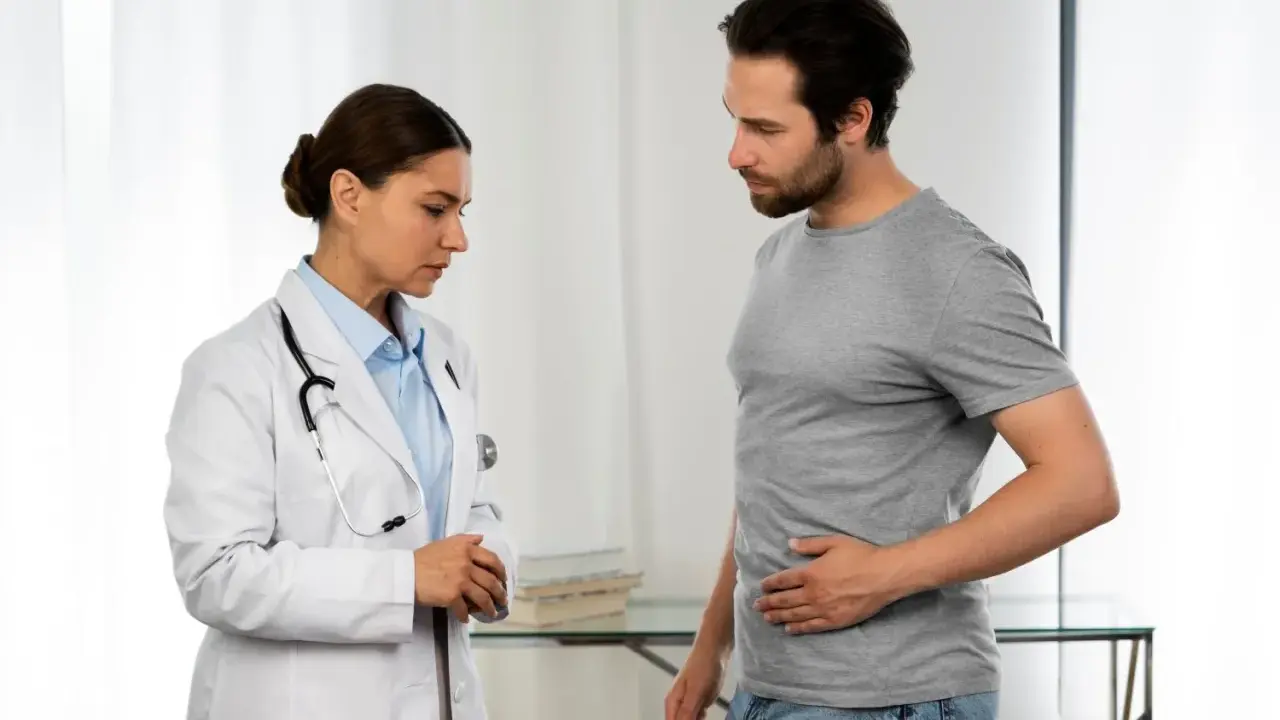 Lekarka w białym kitlu rozmawia z pacjentem, który trzyma się za brzuch. To może być początek rozmowy o tym, jak wygląda badanie urologiczne u mężczyzn.