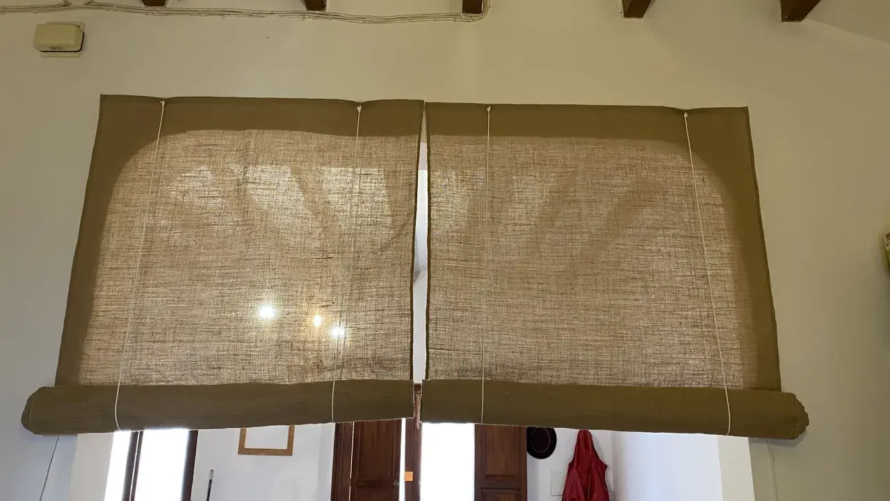 Dos estores enrollables caseros de tela de yute cubren una ventana y una puerta.