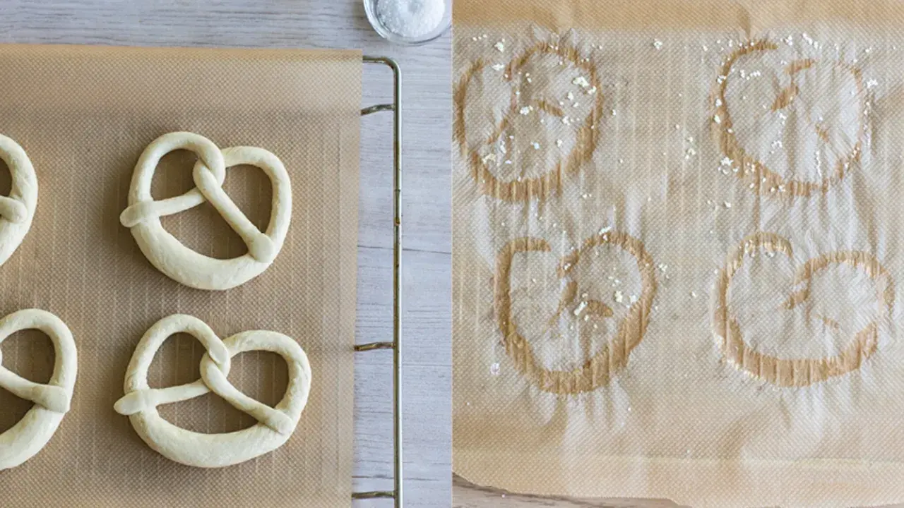 Rohe und gebackene Brezeln auf Backpapier. Links ungeborene, rechts bereits gebackene Brezeln, die zeigen, wie sie aufbacken.