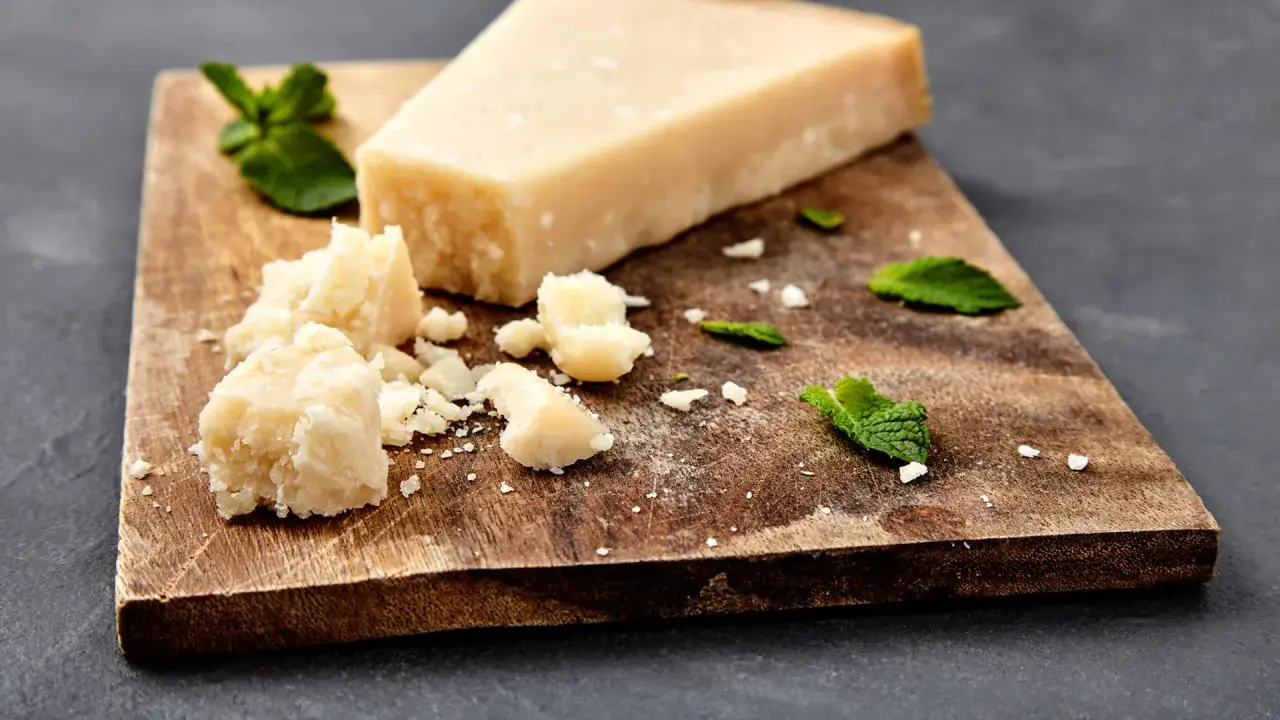 Ein Stück und zerbrochene Stücke von ist parmigiano parmesan liegen auf einem Holzbrett, garniert mit Minzblättern.