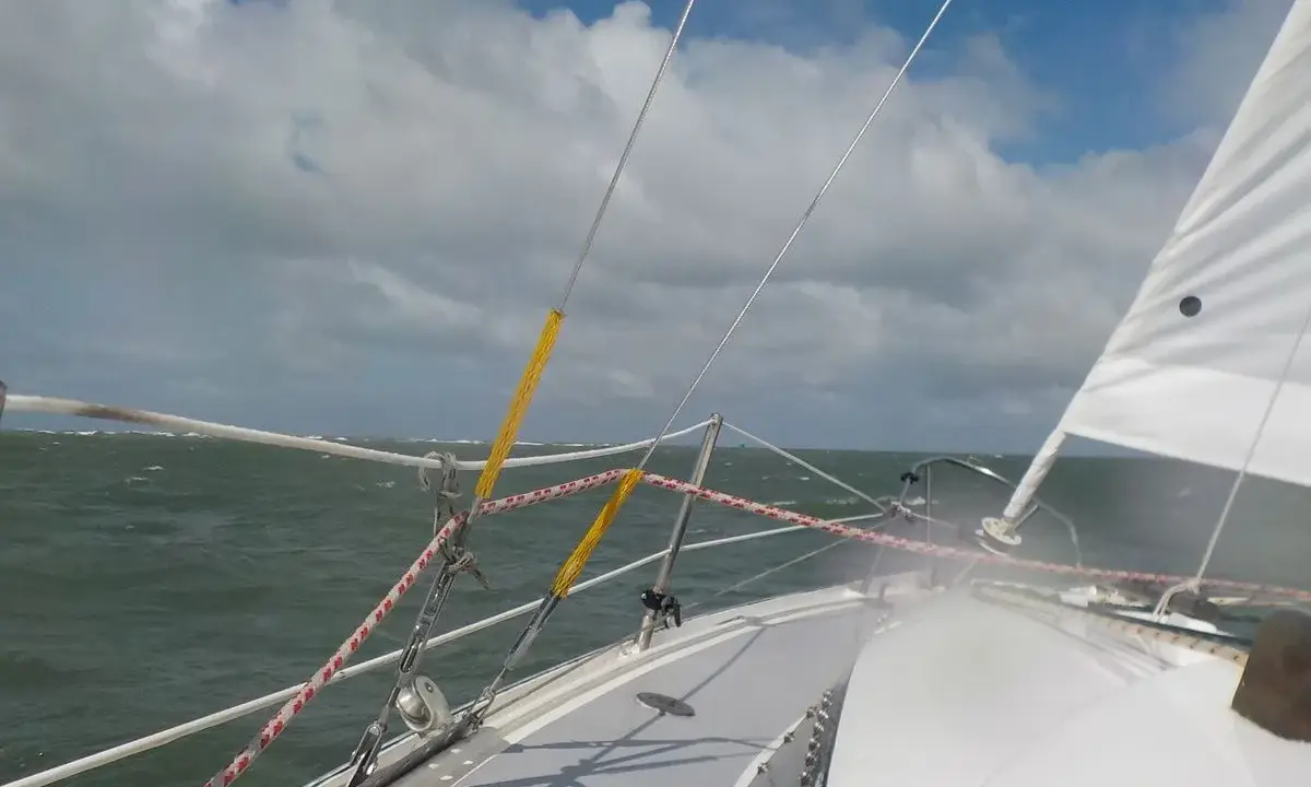 Vue depuis un voilier, mer agitée sous un ciel nuageux. Le gréement et la voile blanche sont visibles. Fiche technique du Challenger Scout.