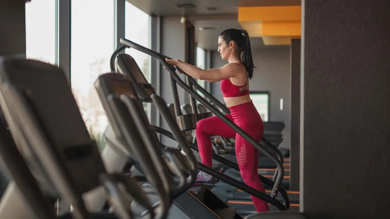 Frau macht ein Stairmaster Workout im Fitnessstudio. Sie trägt ein rotes Sportoutfit und trainiert intensiv.