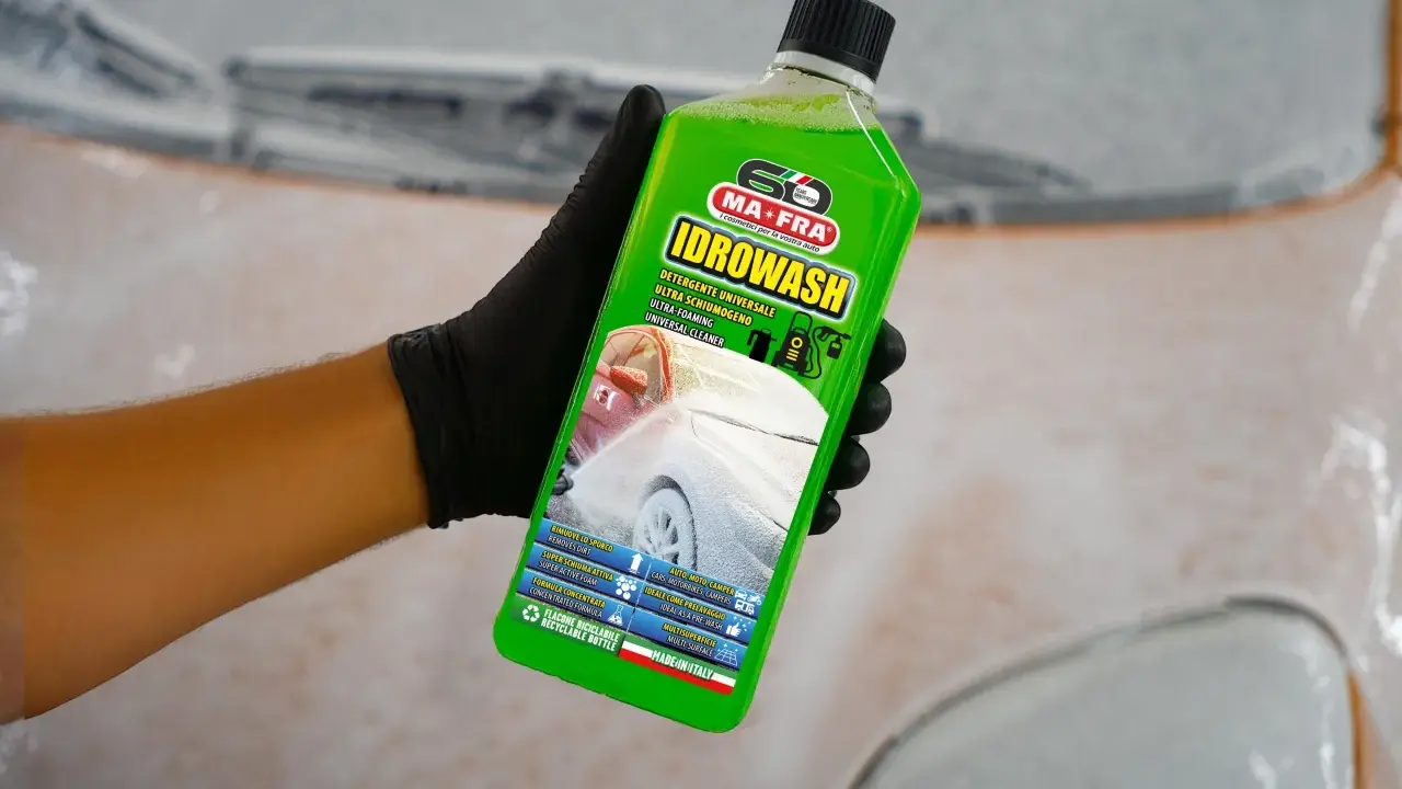 Mano con guanto nero tiene bottiglia di Idrowash, un detergente schiumoso verde brillante per auto.