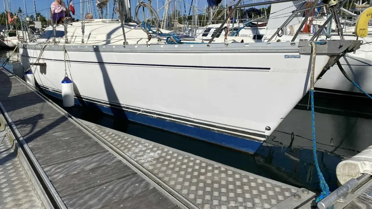 Un voilier blanc est amarré à quai. Le soleil se lève, projetant de longues ombres sur le ponton en bois.