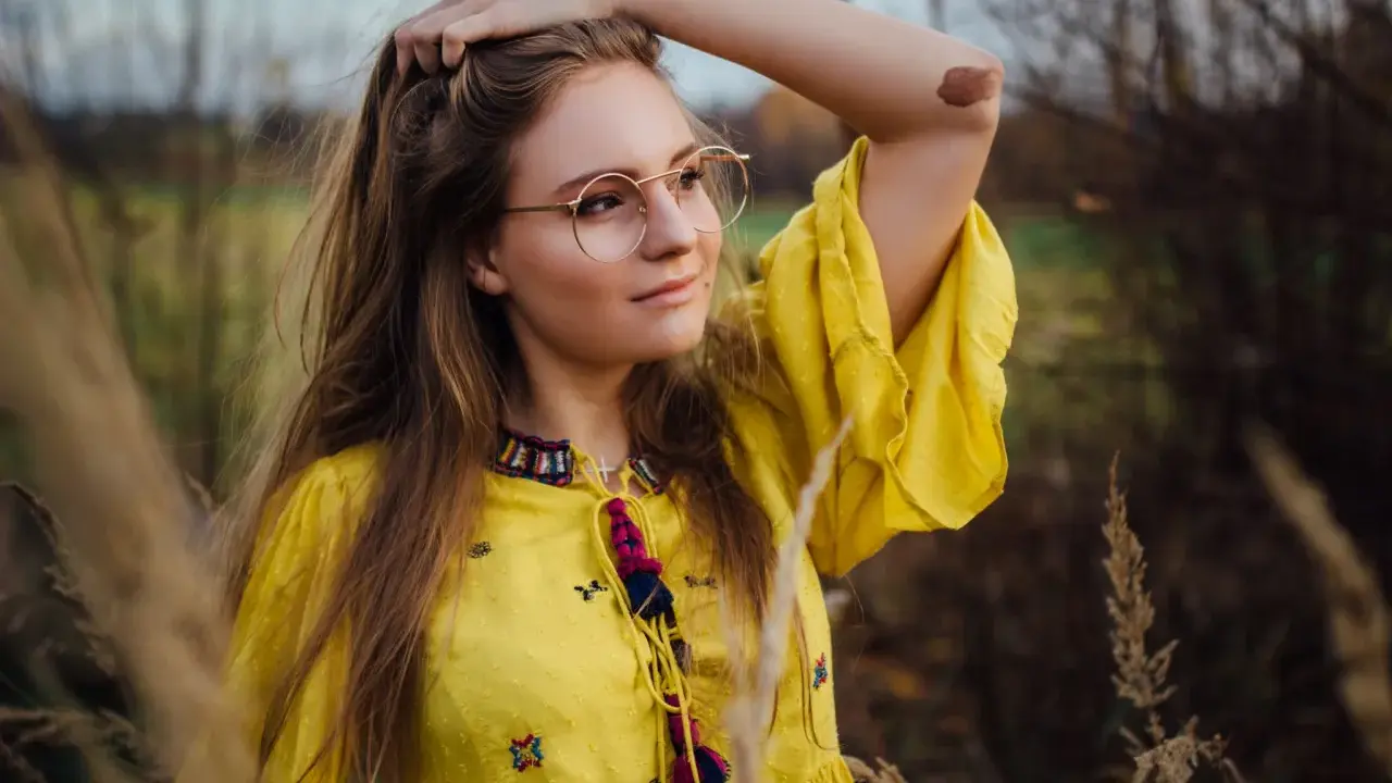 Portret dziewczyny w okularach i żółtej sukience, wśród traw. Różne rodzaje portretów w fotografii mogą uchwycić taką naturalną, swobodną chwilę.