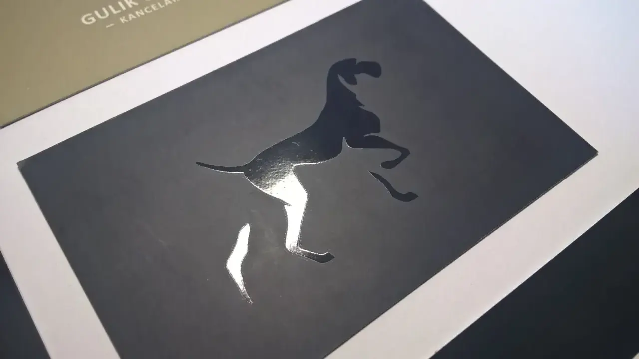 Elegancka wizytówka z psem w skoku, wykonana techniką lakierowania wybiórczego. Błyszczący pies kontrastuje z matowym tłem.