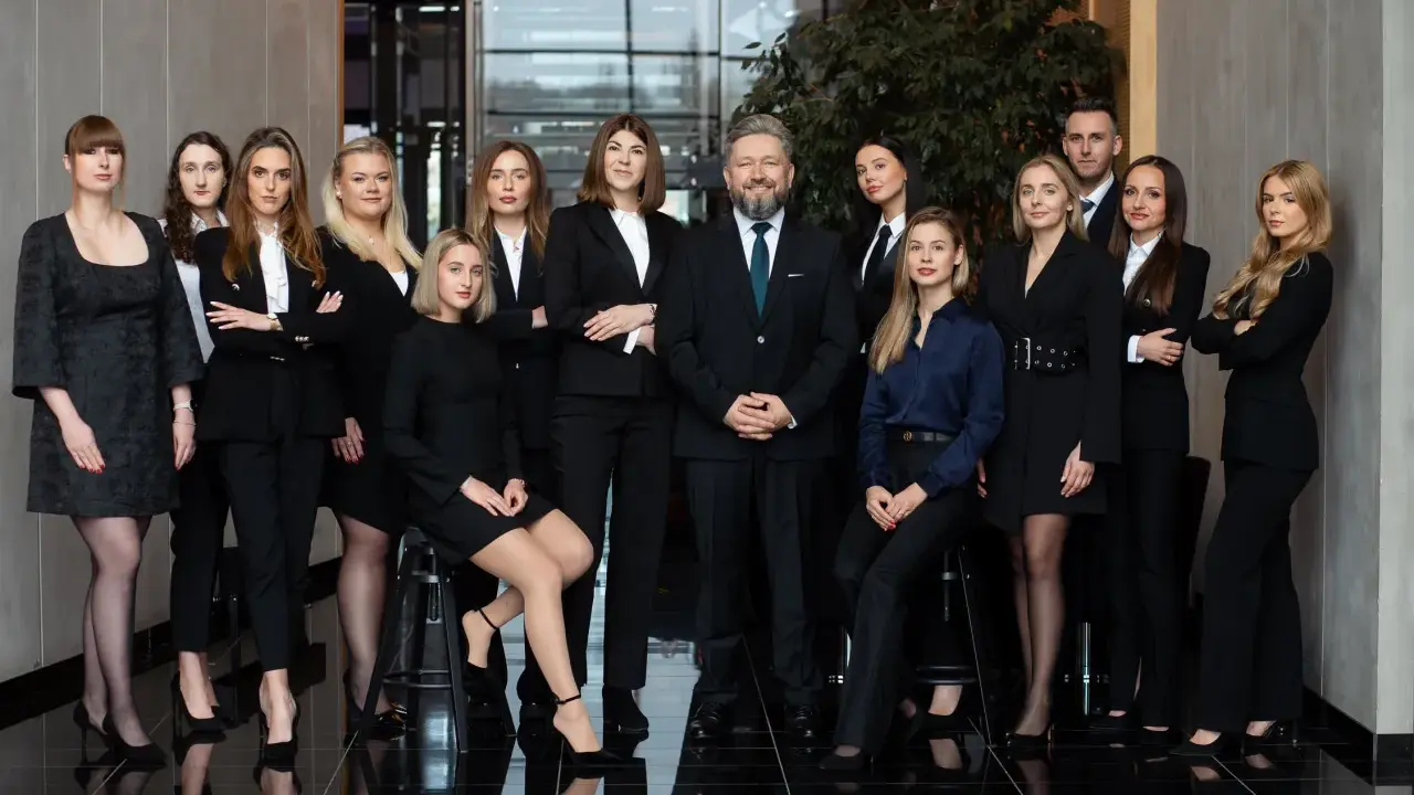 Grupa prawników i adwokatów w eleganckich strojach pozuje do zdjęcia w nowoczesnym wnętrzu.