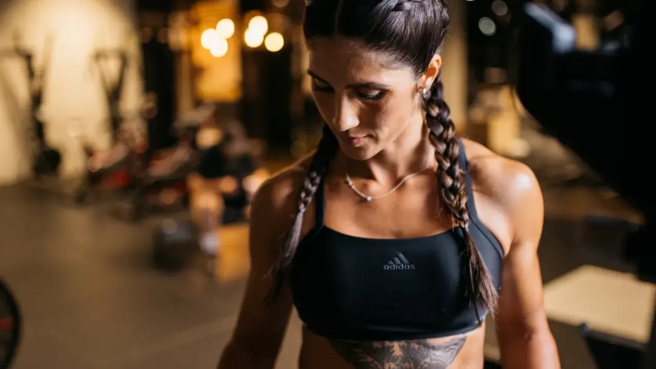 Frau mit geflochtenen Haaren im Fitnessstudio, die ihre definierten Muskeln zeigt.