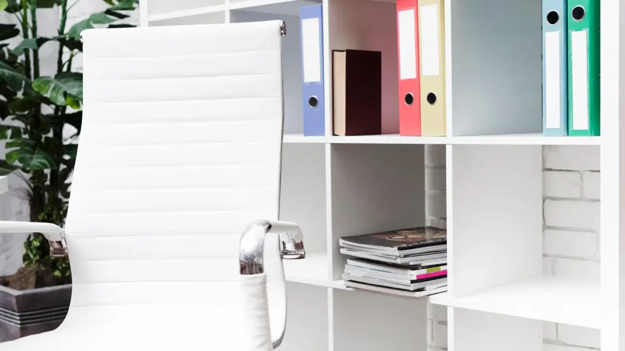 Scrivania ordinata con sedia bianca e scaffali pieni di raccoglitori colorati, perfetti per chi cerca idee su come organizzare i documenti di casa.