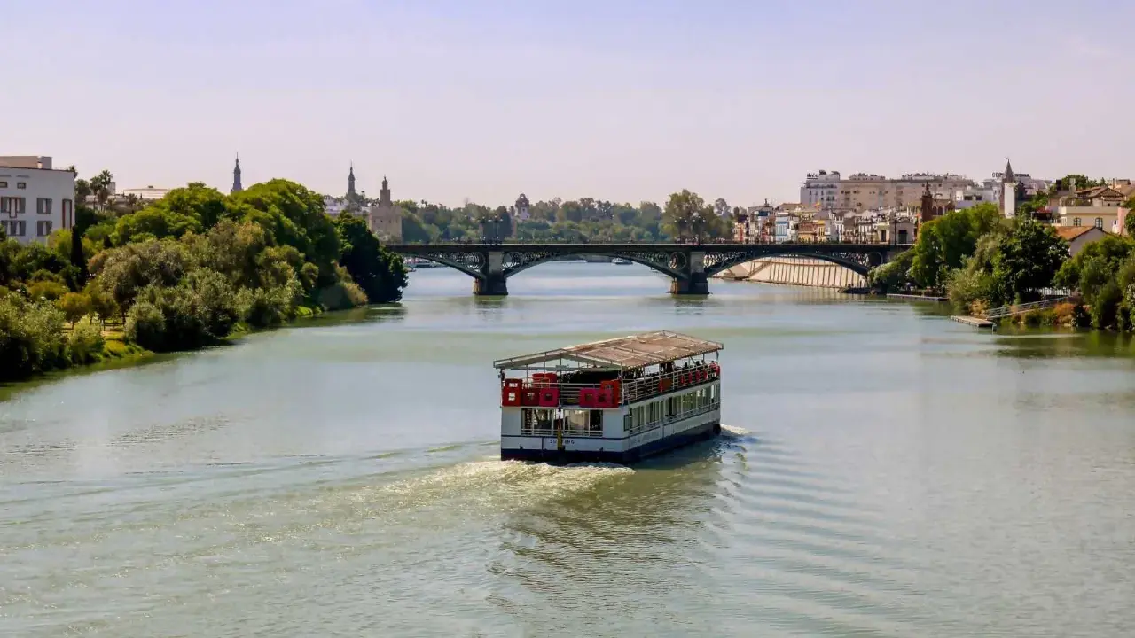 Ein Ausflugsboot fährt auf dem Guadalquivir, dem sevilla fluss, unter einer Brücke hindurch.