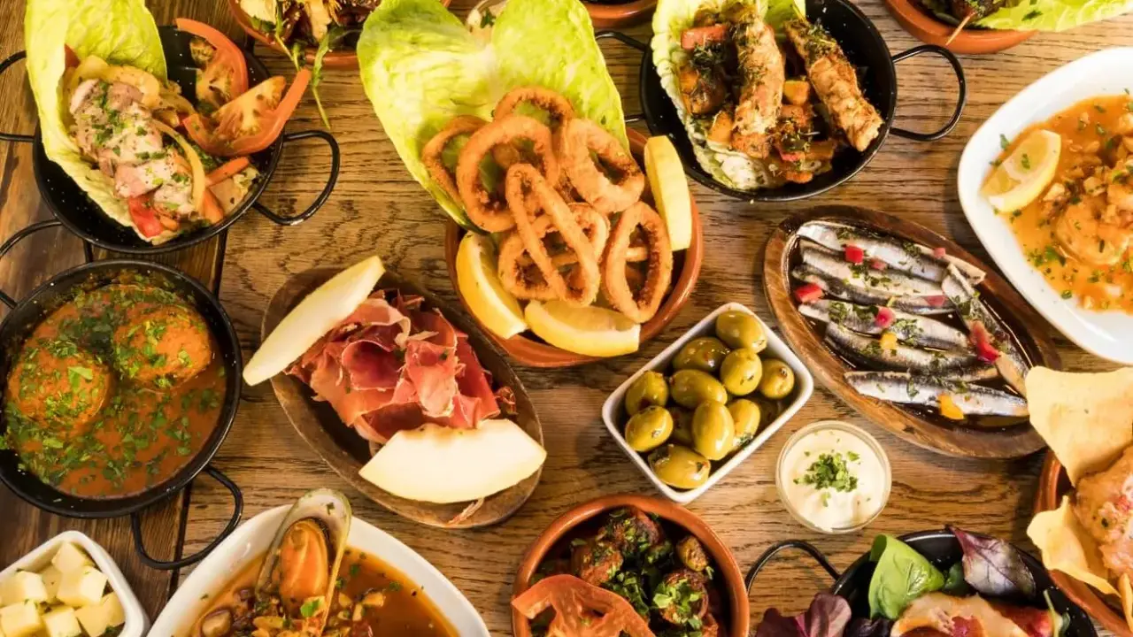 Vielfältige Tapas ideen: Tintenfischringe, Sardinen, Garnelen, Fleischbällchen, Schinken mit Melone, Oliven und mehr auf Holztisch.