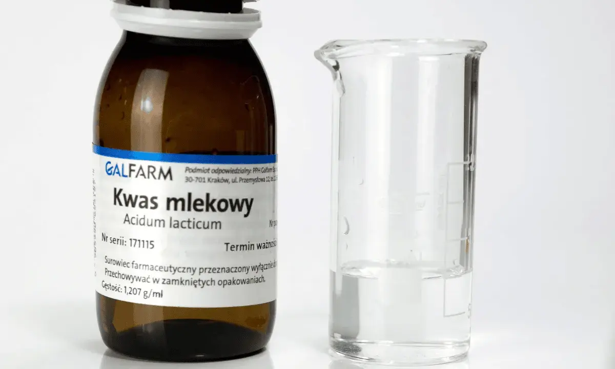 Butelka z napisem "Kwas mlekowy" i zlewka z płynem. Czy kwas mlekowy jest szkodliwy? Zależy od stężenia i zastosowania.