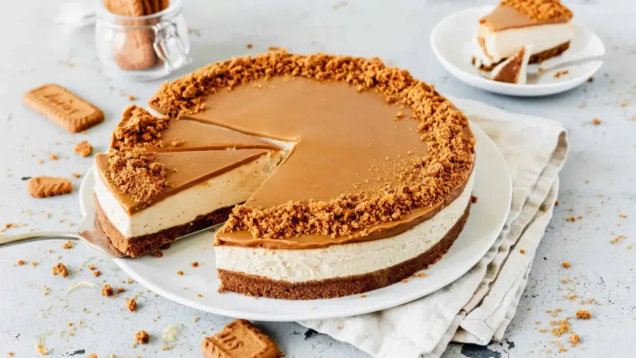 Ein köstlicher Lotus Cheesecake mit Karamellglasur und Keksbröseln. Ein Stück wurde bereits entnommen, daneben liegen weitere Kekse.