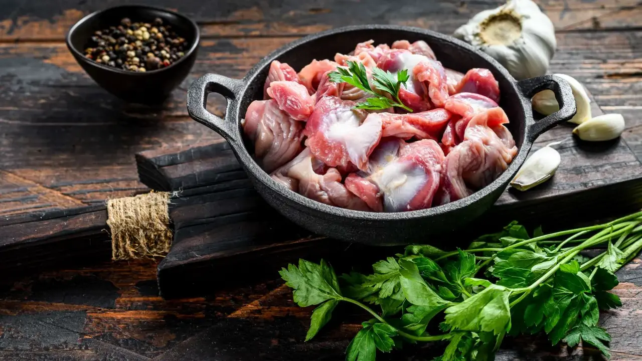 Piatto toscano con interiora di pollo crude in padella, con aglio, pepe e prezzemolo su tagliere di legno scuro.