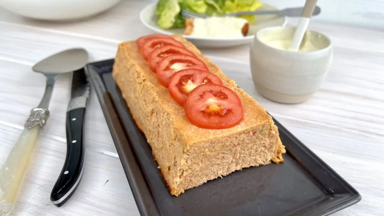 Un pain de thon savoureux, garni de rondelles de tomate fraîche, prêt à être dégusté avec une salade verte et une sauce crémeuse.