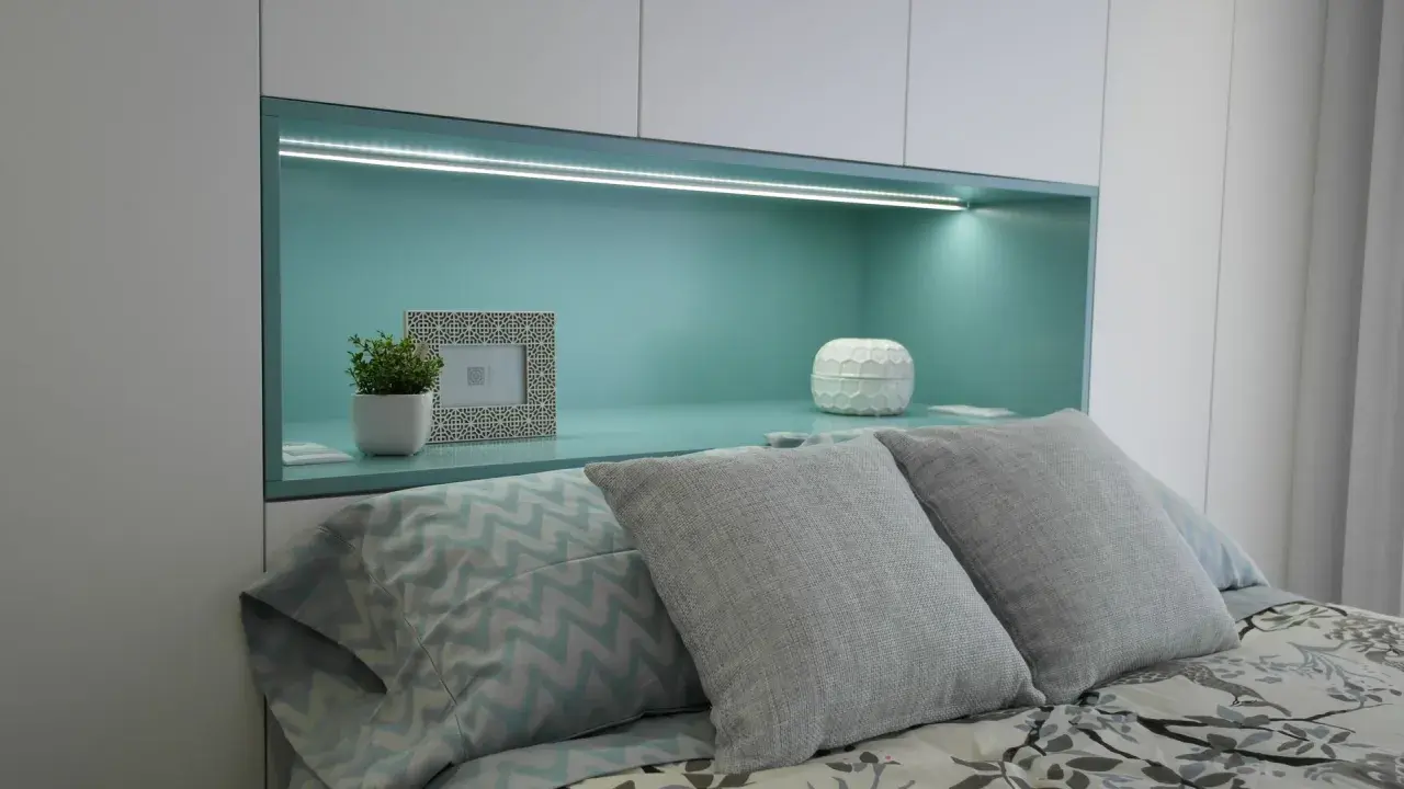 Habitación verde pistacho y gris con cama, almohadas y nicho iluminado.