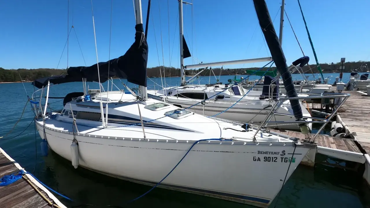 Voilier Beneteau First 235 blanc amarré à un ponton en bois, avec voiles noires et bleues.