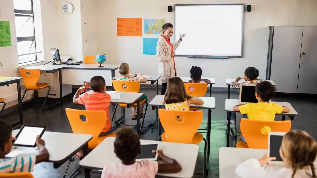 Nauczycielka prowadzi lekcję w klasie pełnej dzieci. To idealne miejsce do nauki pedagogiki przedszkolnej i wczesnoszkolnej w Poznaniu.