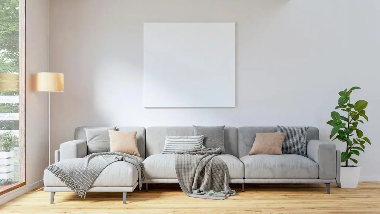 Sofá gris con cojines en tonos tierra y grises, mantas y planta. El color de cojines para sofá gris ideal para un ambiente acogedor.