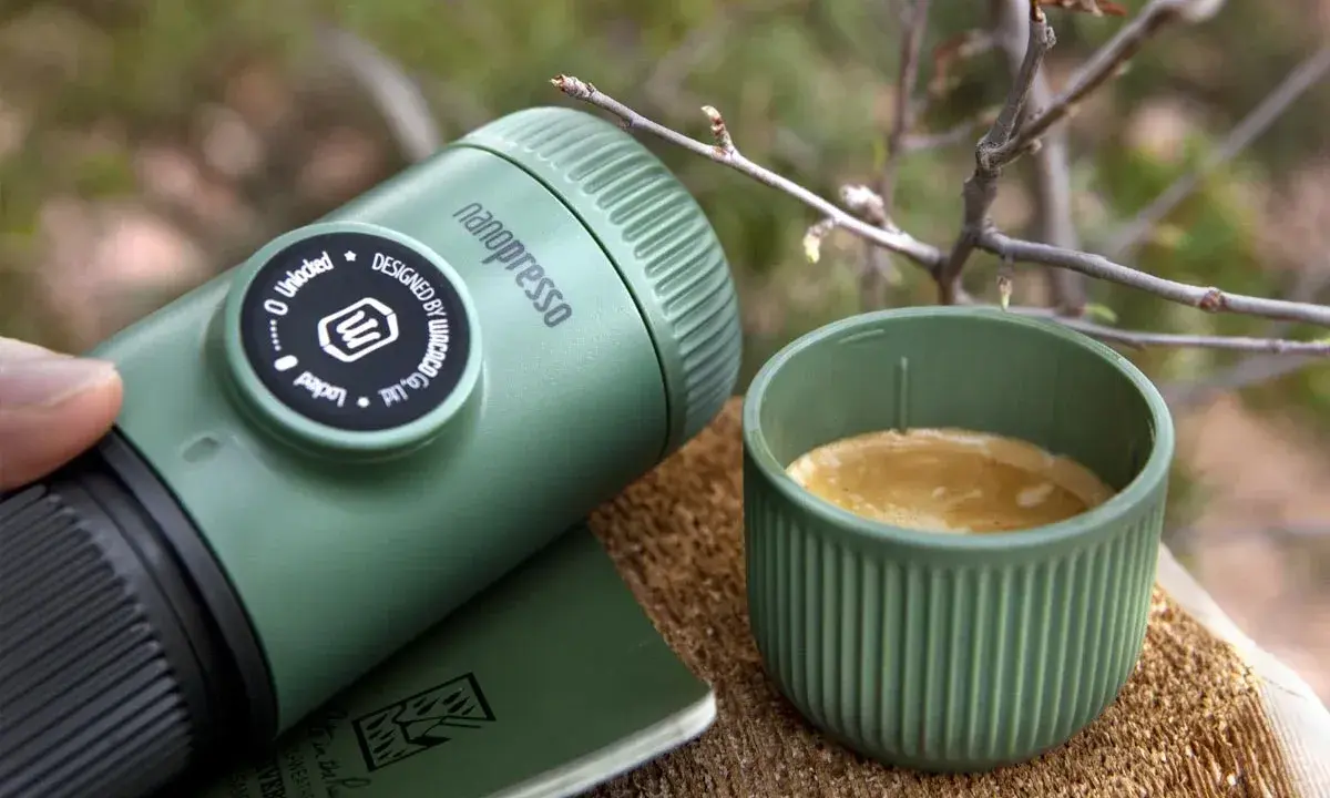 Zielona kawa w górach. Nanopresso i kubek z aromatycznym espresso na drewnianym pniu, wśród gałązek. Idealny towarzysz podróży.