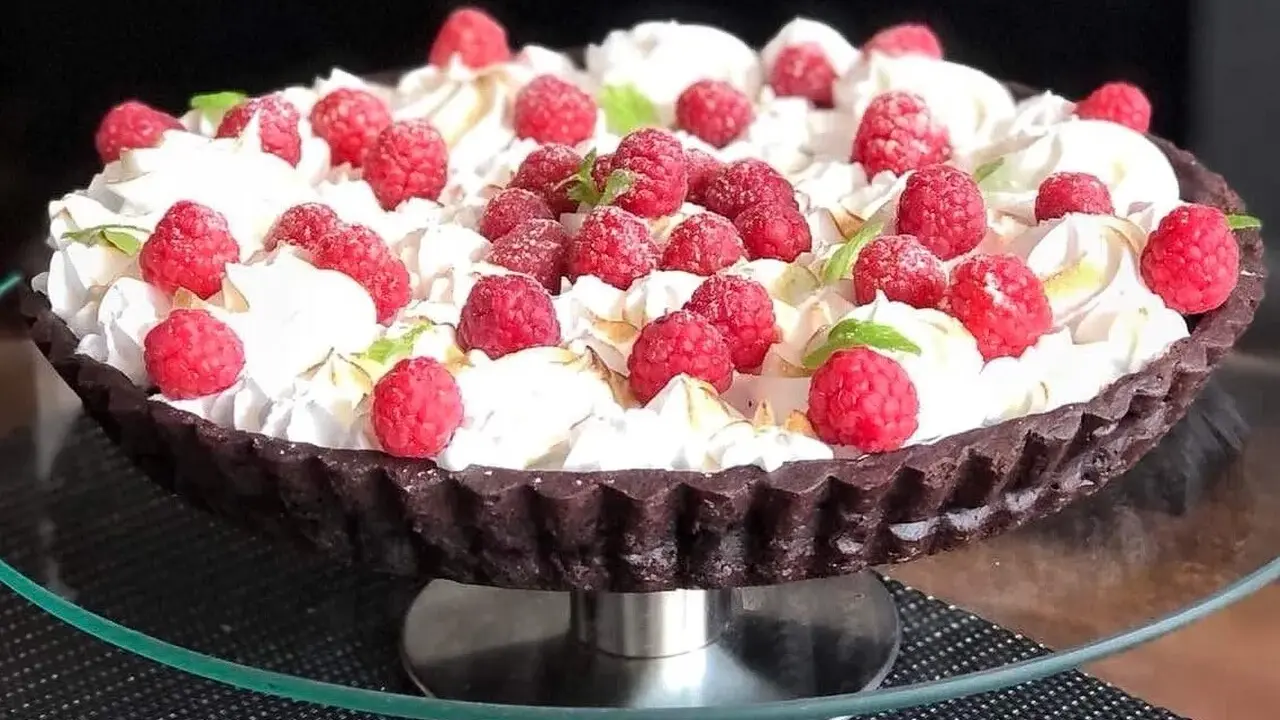 Pyszna tarta czekoladowa z malinami, udekorowana bitą śmietaną i listkami mięty. Idealna na deser.