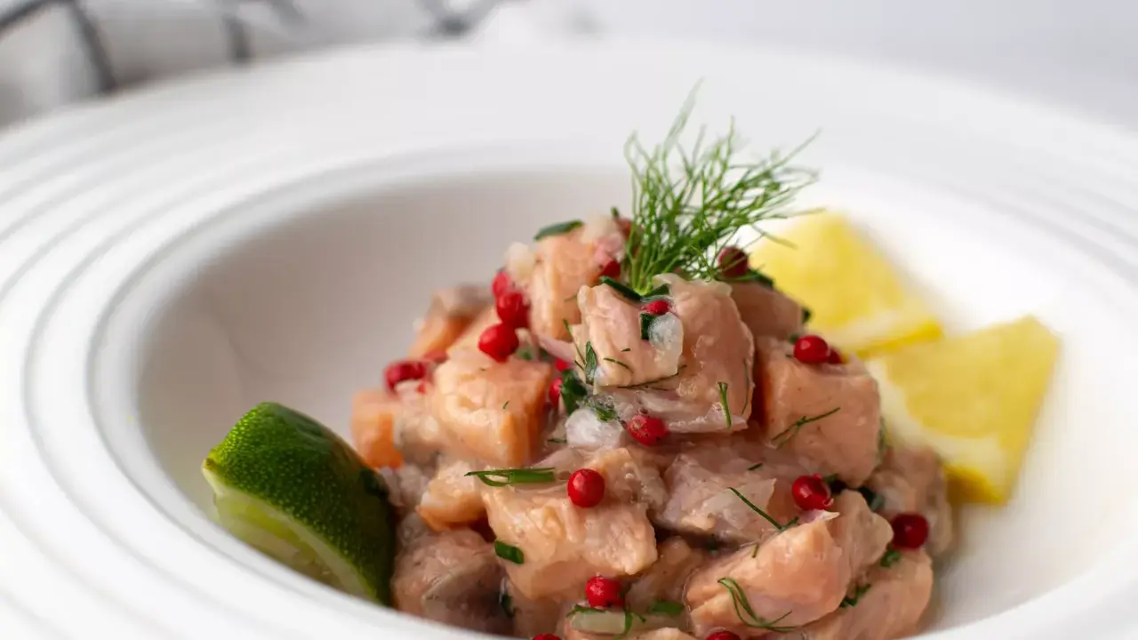 Un classique tartare de saumon, frais et coloré, garni d'aneth, de baies roses et servi avec des quartiers de citron vert et de citron jaune.