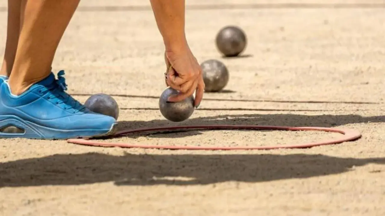 Une main saisit une boule de pétanque, prête à la lancer dans le cercle. Les règles du jeu de boules sont simples : viser le cochonnet.