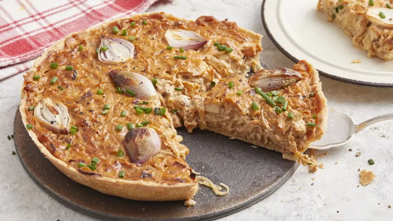 Une délicieuse tarte à l'oignon, garnie d'oignons caramélisés et de ciboulette fraîche, est prête à être dégustée. Une part est servie sur une assiette.