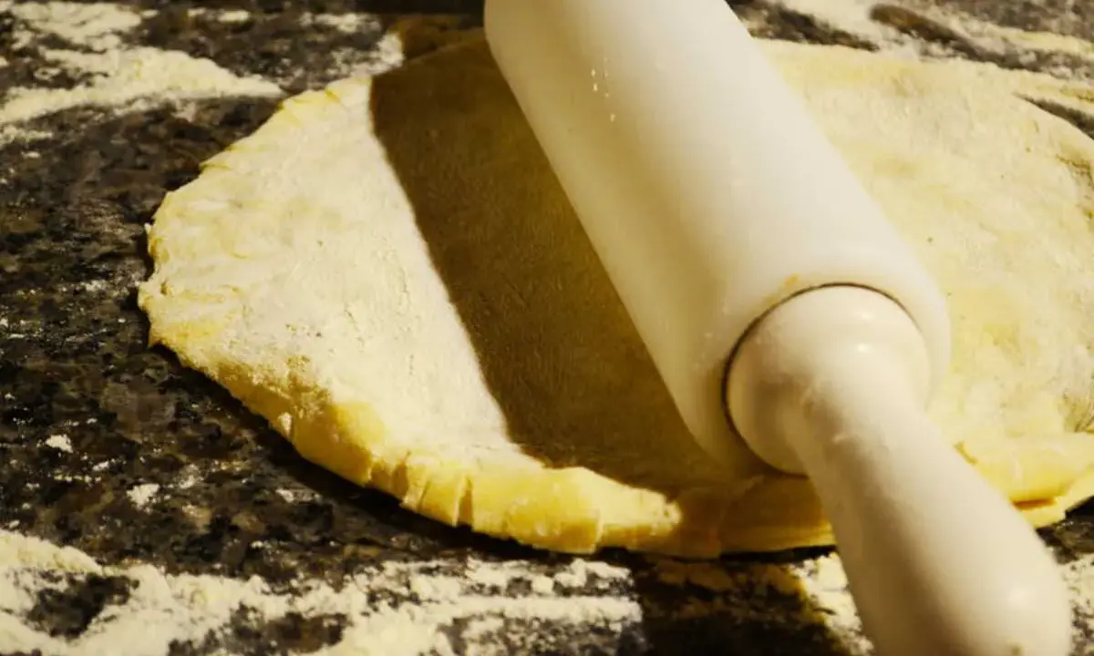 Rouleau à pâtisserie aplatissant une pâte à foncer sur un plan de travail fariné.