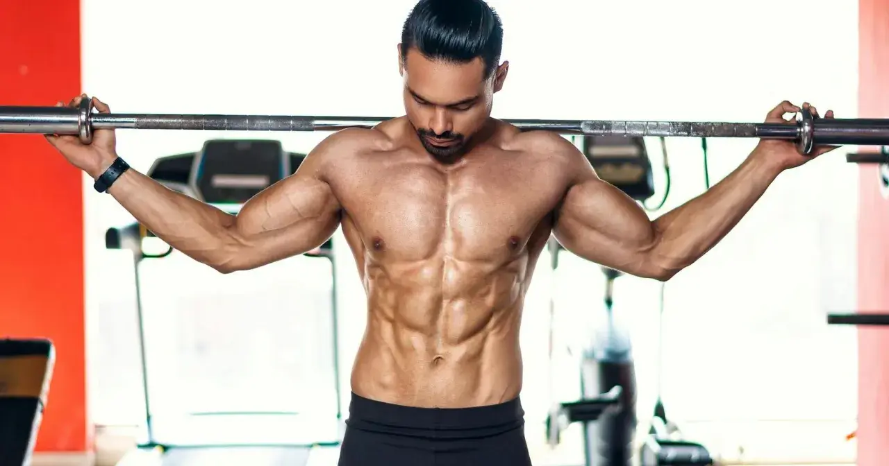 Ein Mann mit stark definierten Bauchmuskeln hält eine Langhantel im **cutten gym**.