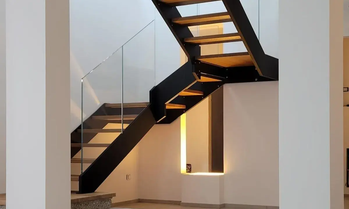 Scala interna con gradini in legno e struttura metallica nera. Il parapetto in vetro trasparente dona leggerezza al design moderno.