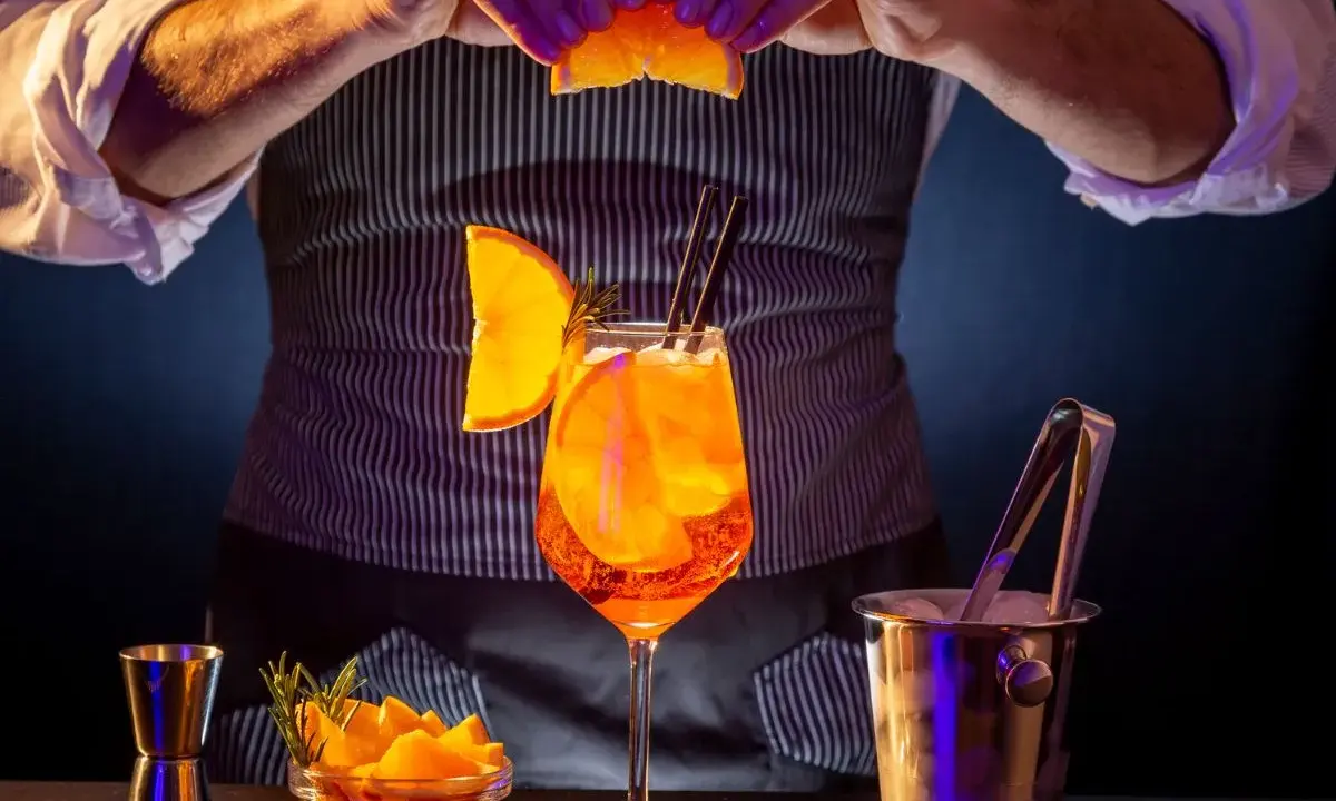 Barman prepara un Aperol Spritz, mostrando los distintos tipos de aperol y sus guarniciones.